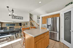 Kitchen with stainless steel refrigerator with ice dispenser, a center island, light tile patterned flooring, lofted ceiling, and a breakfast bar area