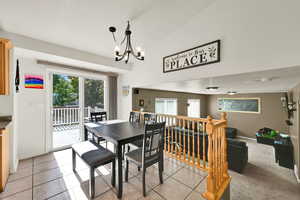 Dining area with a textured ceiling, light tile patterned flooring, vaulted ceiling, a chandelier, and light colored carpet