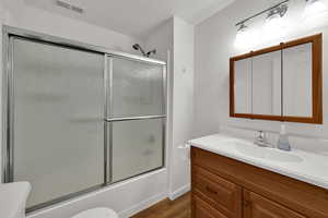 Bathroom featuring bath / shower combo with glass door, vanity, and dark wood-style flooring