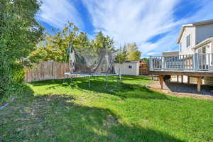 Fenced backyard with a storage unit, a deck, and a trampoline