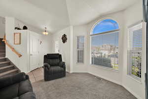 Tiled living room featuring carpet flooring, stairs, healthy amount of natural light, a textured ceiling, and vaulted ceiling
