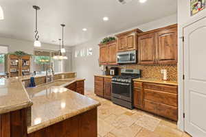 Kitchen with stainless steel appliances, pendant lighting, brown cabinets, decorative backsplash, and light stone countertops