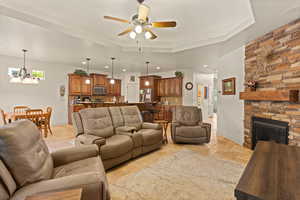 Living room with a stone fireplace, stone tile flooring, ceiling fan, recessed lighting, and a tray ceiling