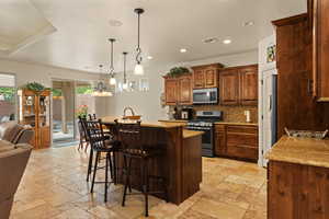 Kitchen featuring a breakfast bar, an island with sink, appliances with stainless steel finishes, pendant lighting, and decorative backsplash