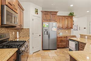 Kitchen with stainless steel appliances, light stone counters, brown cabinets, tasteful backsplash, and recessed lighting