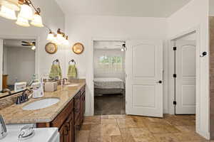 Ensuite bathroom with double vanity, ceiling fan, stone tile floors, and a chandelier
