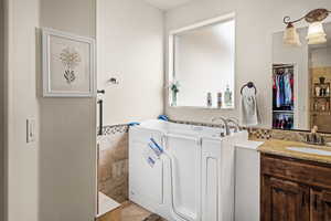 Full bath with tile walls, vanity, a garden tub, a walk in closet, and wainscoting