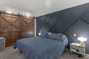 Bedroom featuring light carpet, vaulted ceiling, and a decorative wall