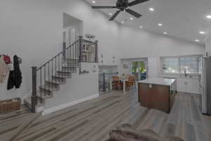 Kitchen featuring a kitchen island, high vaulted ceiling, recessed lighting, light wood-style flooring, and white cabinets