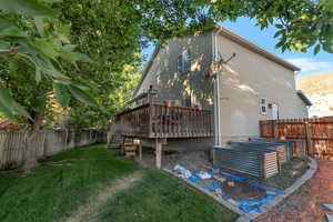 View of side of home with a fenced backyard, a deck with mountain view, stucco siding, a garden, and stairs