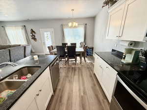 Kitchen featuring white cabinets, dark stone countertops, stainless steel appliances, light wood-style floors, and open floor plan