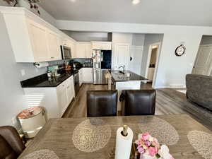 Kitchen with appliances with stainless steel finishes, a center island with sink, dark wood-style floors, dark stone countertops, and recessed lighting