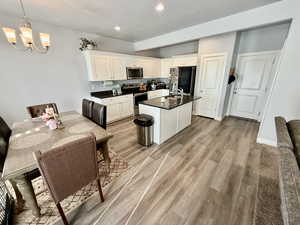 Kitchen with stainless steel appliances, light wood finished floors, white cabinetry, dark stone counters, and recessed lighting