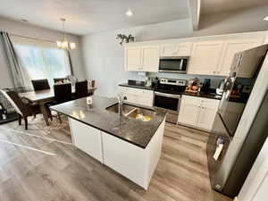 Kitchen with appliances with stainless steel finishes, white cabinets, light wood-style flooring, hanging light fixtures, and recessed lighting