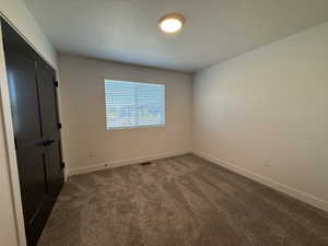Unfurnished bedroom with dark colored carpet, a closet, and a textured ceiling