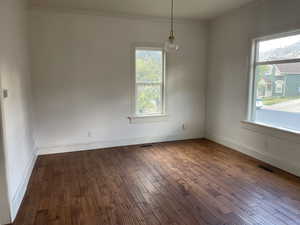 Empty room featuring healthy amount of natural light, ornamental molding, and dark wood-type flooring