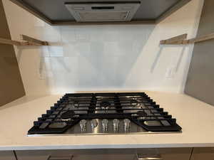 Kitchen view of light stone counters, stainless steel gas stovetop, extractor fan, and backsplash