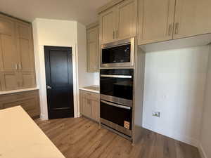 Kitchen with appliances with stainless steel finishes, light wood-style flooring, and light stone counters