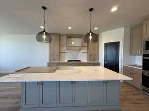 Kitchen featuring light wood-type flooring, light stone countertops, tasteful backsplash, decorative light fixtures, and recessed lighting