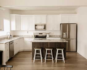 Kitchen featuring appliances with stainless steel finishes, white cabinets, light stone counters, and a breakfast bar area