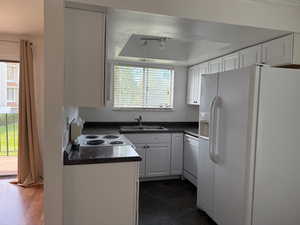 Kitchen with white appliances, dark countertops, white cabinetry, and a tray ceiling