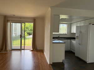 Kitchen with white cabinetry, white appliances, dark countertops, ornamental molding, and dark wood-type flooring