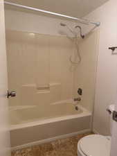 Bathroom featuring washtub / shower combination, a textured ceiling, and light tile patterned floors
