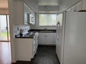 Kitchen with white appliances, white cabinetry, healthy amount of natural light, dark countertops, and a textured ceiling