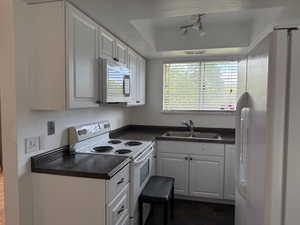 Kitchen featuring white appliances, dark countertops, a tray ceiling, and white cabinetry