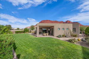 Back of house with stucco siding, a lawn, and a patio