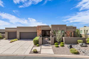 Adobe home featuring a gate, stone siding, stucco siding, a fenced front yard, and concrete driveway