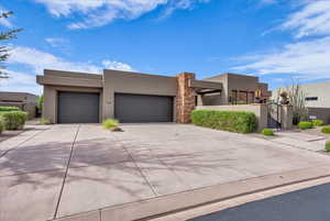 Pueblo-style home featuring stucco siding, a gate, a garage, concrete driveway, and stone siding