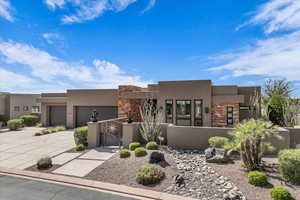 Pueblo-style home featuring stone siding, stucco siding, driveway, a fenced front yard, and a garage