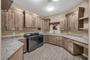 Laundry area with light wood finished floors, cabinet space, washer and dryer, and a textured ceiling