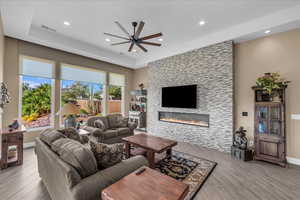Living room with a ceiling fan, a large fireplace, light wood finished floors, recessed lighting, and a tray ceiling
