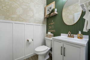 Half bath with vanity, wood finished floors, wallpapered walls, and a decorative wall