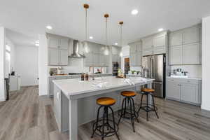 Kitchen featuring gray cabinetry, appliances with stainless steel finishes, hanging light fixtures, a breakfast bar area, and tasteful backsplash