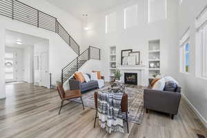 Living room featuring a towering ceiling, a glass covered fireplace, stairway, light wood-style flooring, and built in features