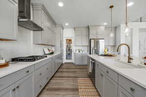 Kitchen with gray cabinets, stainless steel appliances, wall chimney exhaust hood, light wood-style flooring, and recessed lighting