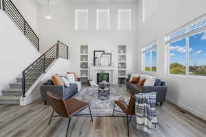 Living area featuring a towering ceiling, a fireplace, stairway, light wood-style floors, and built in shelves