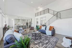 Living room with a high ceiling, stairway, light wood-style flooring, and recessed lighting
