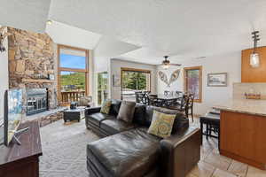 Living area with a ceiling fan, a stone fireplace, and a textured ceiling