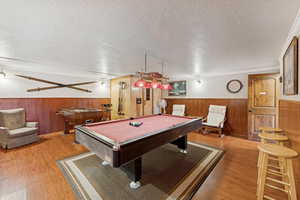 Playroom featuring wooden walls, wainscoting, pool table, wood finished floors, and a textured ceiling