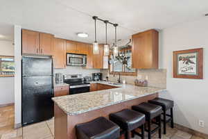 Kitchen featuring appliances with stainless steel finishes, a peninsula, a kitchen breakfast bar, light stone countertops, and a textured ceiling