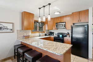 Kitchen with a peninsula, black appliances, a kitchen breakfast bar, and backsplash