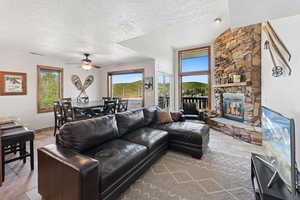 Living room with a textured ceiling, a stone fireplace, ceiling fan, and light tile patterned flooring