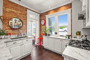 Kitchen featuring white cabinetry, brick wall, dark wood-style flooring, ornamental molding, and hanging light fixtures