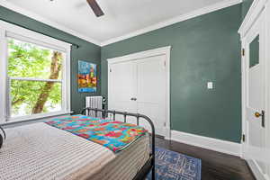 Bedroom with crown molding, dark wood-type flooring, radiator heating unit, a closet, and a ceiling fan