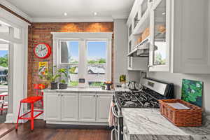 Kitchen featuring white cabinetry, stainless steel range with gas stovetop, glass insert cabinets, brick wall, and dark wood-style floors