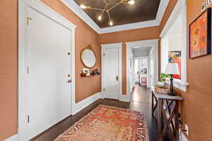 Foyer with ornamental molding, a chandelier, and dark wood finished floors